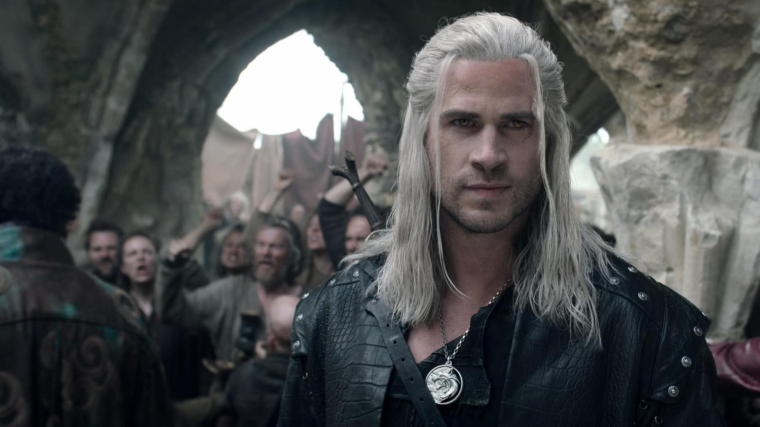 Liam Hemsworth as Geralt of Rivia in The Witcher Season 4, wearing armor and wielding a sword.