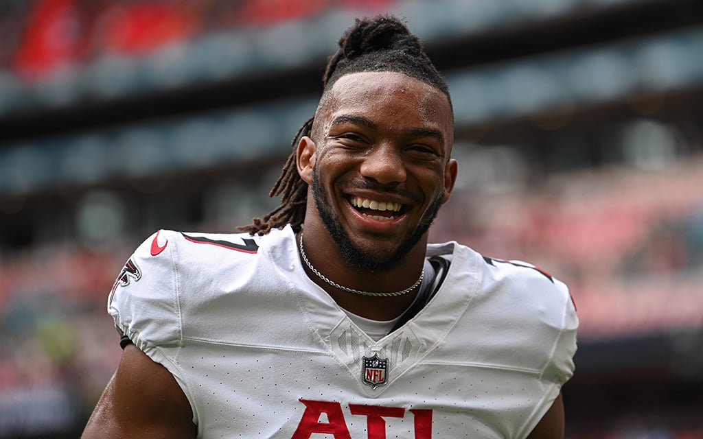 Bijan Robinson smiling at the camera while on the football field during a game.