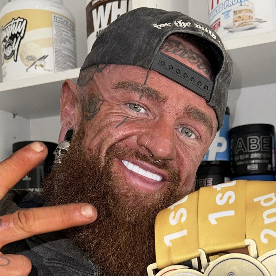 DemonDean, Scottish TikTok fitness influencer, posing in his home gym with championship medals and supplement bottles in the background.
