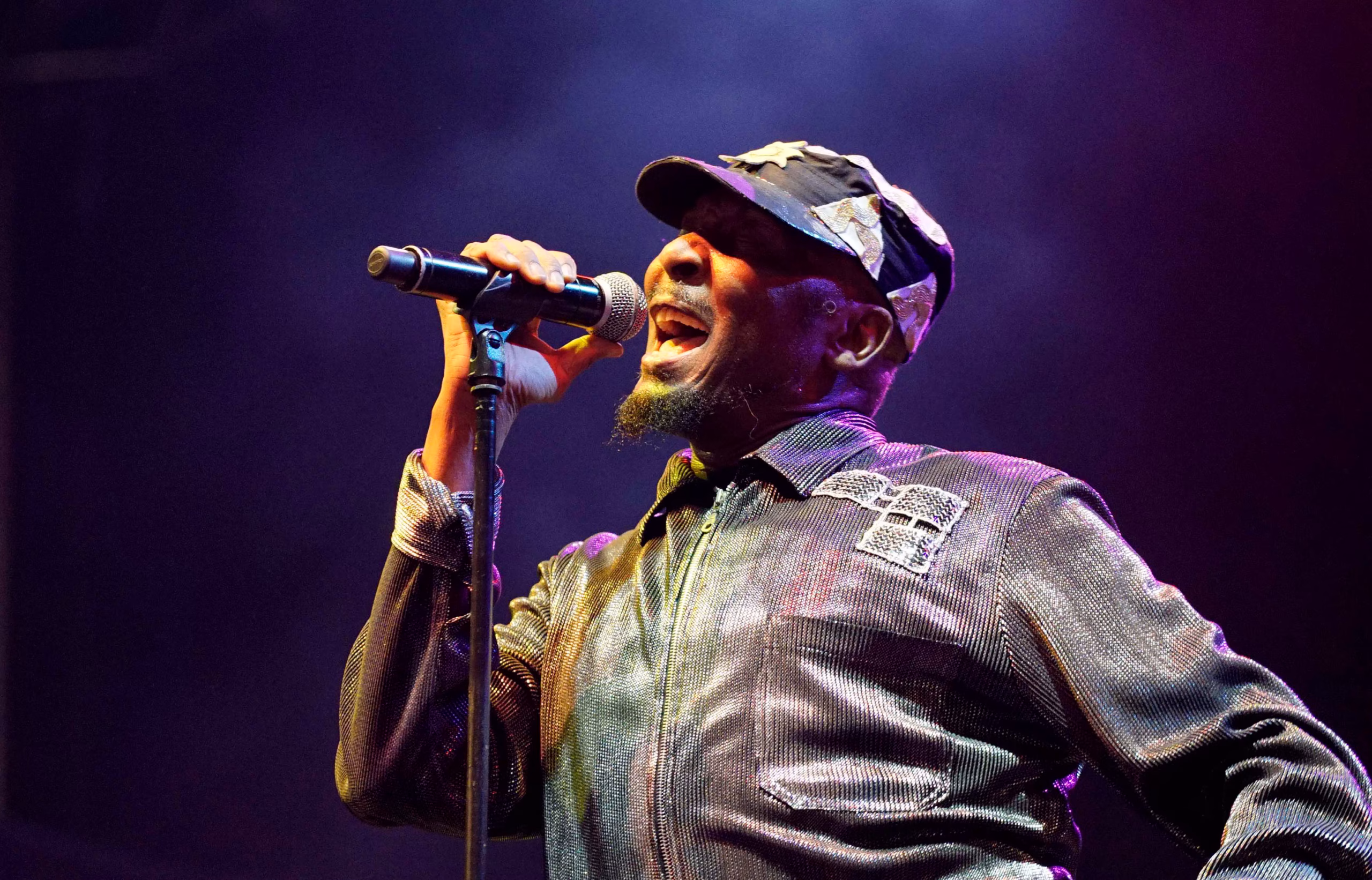 Jimmy Cliff performing on stage, passionately singing into the microphone as the crowd cheers.