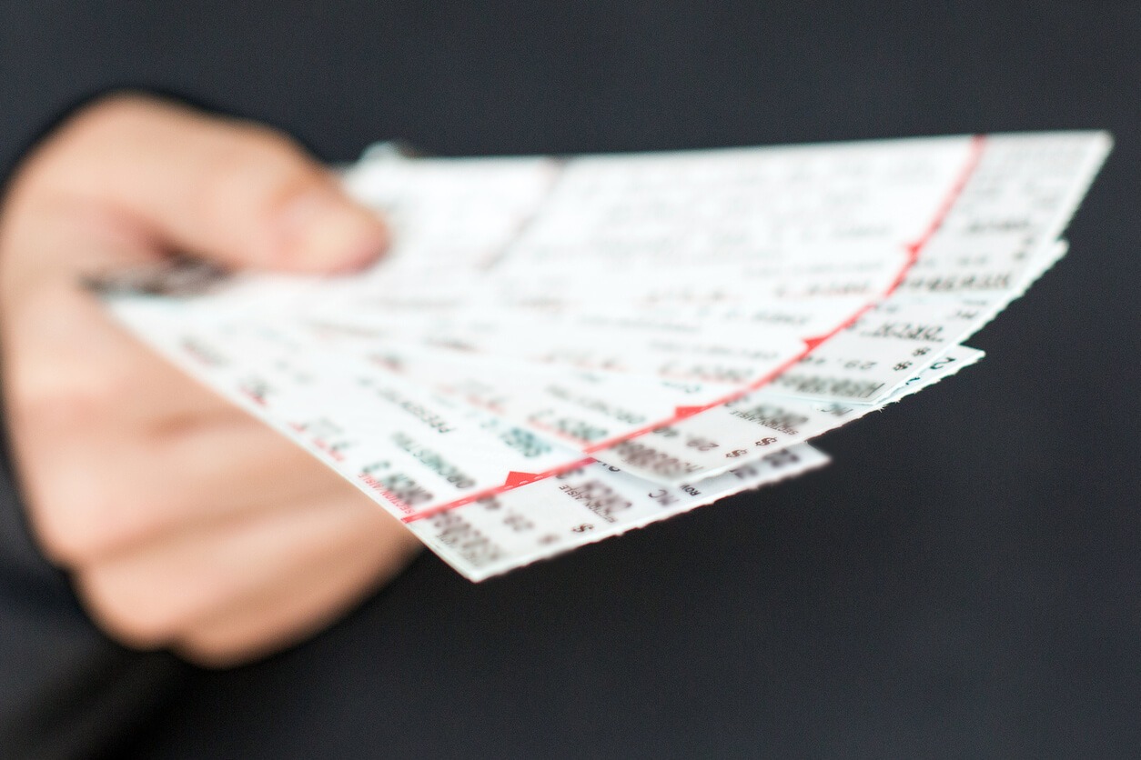 A hand holding a stack of concert tickets, representing ticket touts reselling at inflated prices.