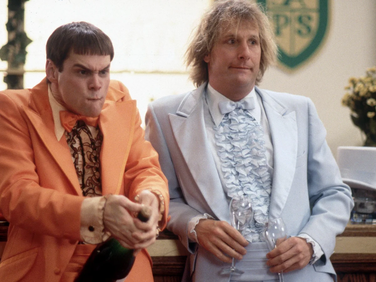 Jim Carrey and Jeff Daniels in character as Lloyd Christmas and Harry Dunne in Dumb and Dumber, wearing their iconic mismatched suits.
