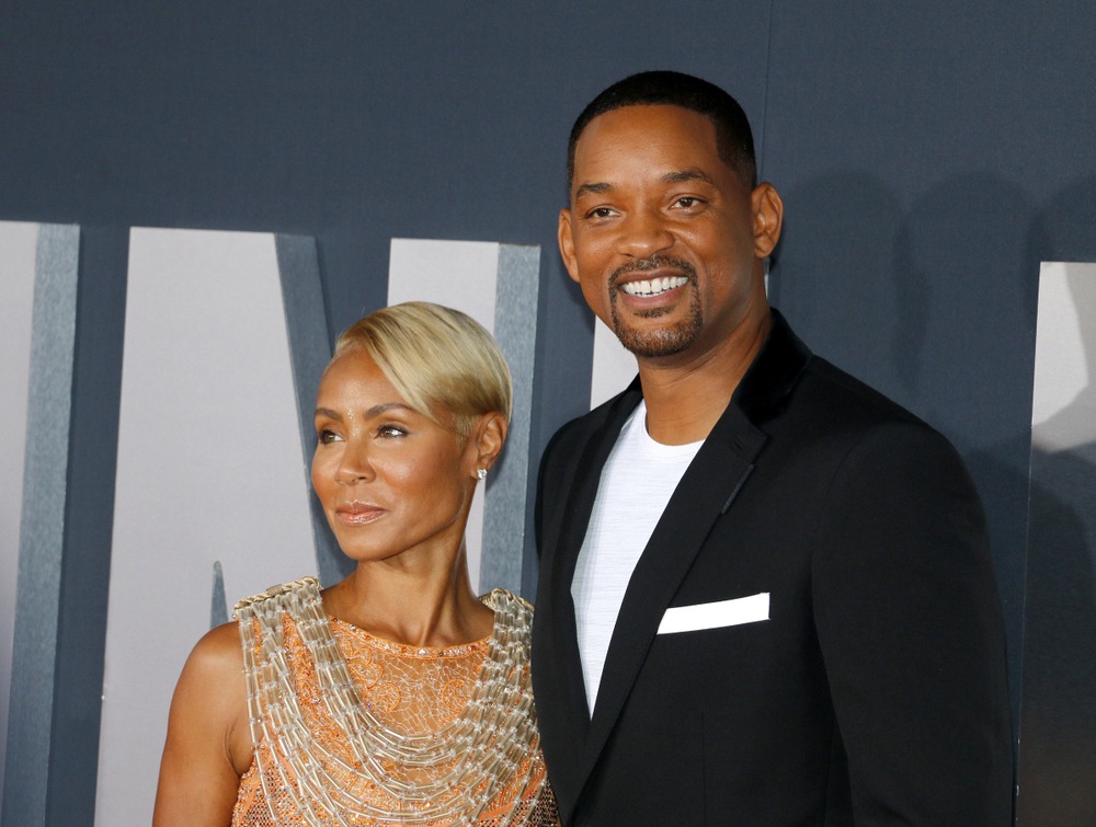 Jada Pinkett Smith and Will Smith smiling together on the red carpet, radiating charm and celebrity glamour.
