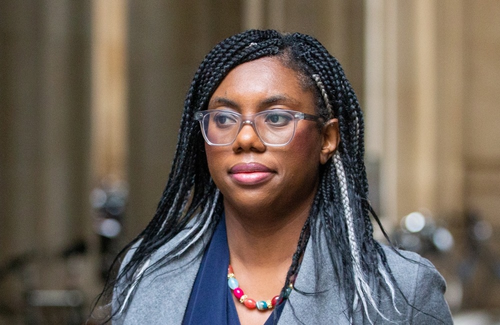 Kemi Badenoch smiling as she walks out of the Houses of Parliament, wearing a smart coat.