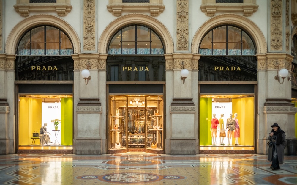 Exterior of a modern Prada store with sleek black signage and minimalist architectural design, symbolising Prada’s expanding global presence following its acquisition of Versace.