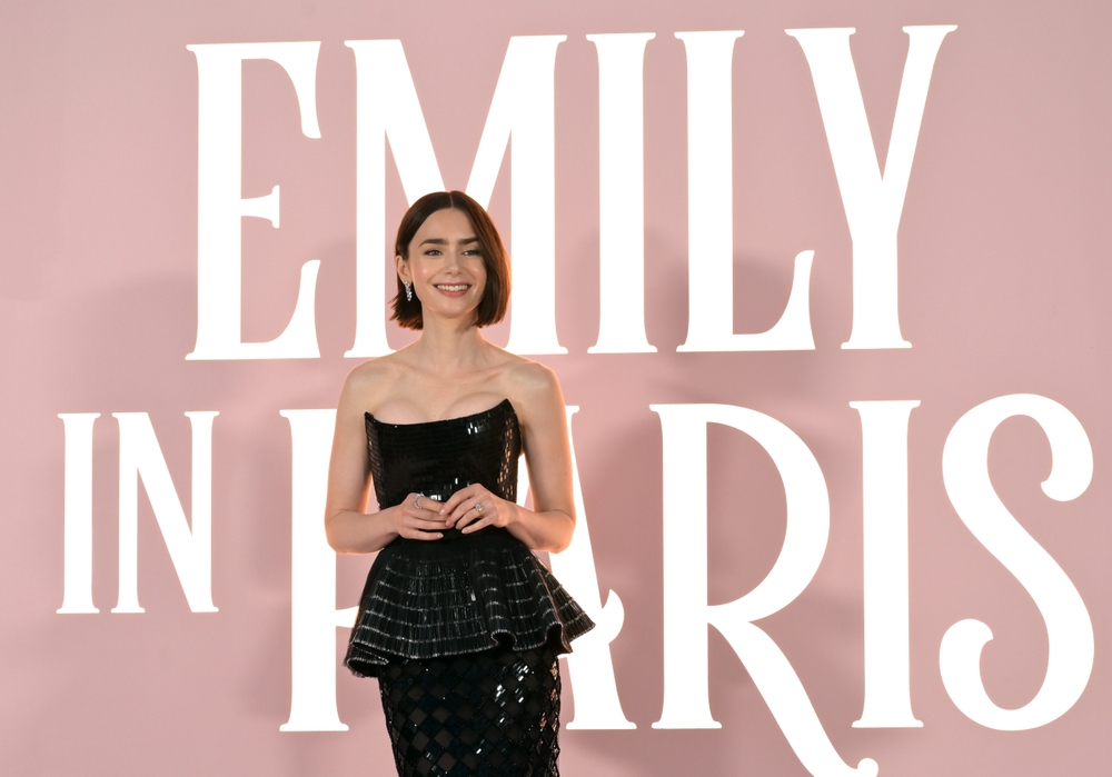 Lily Collins smiling on the red carpet at a past event, wearing an elegant gown and posing for photographers