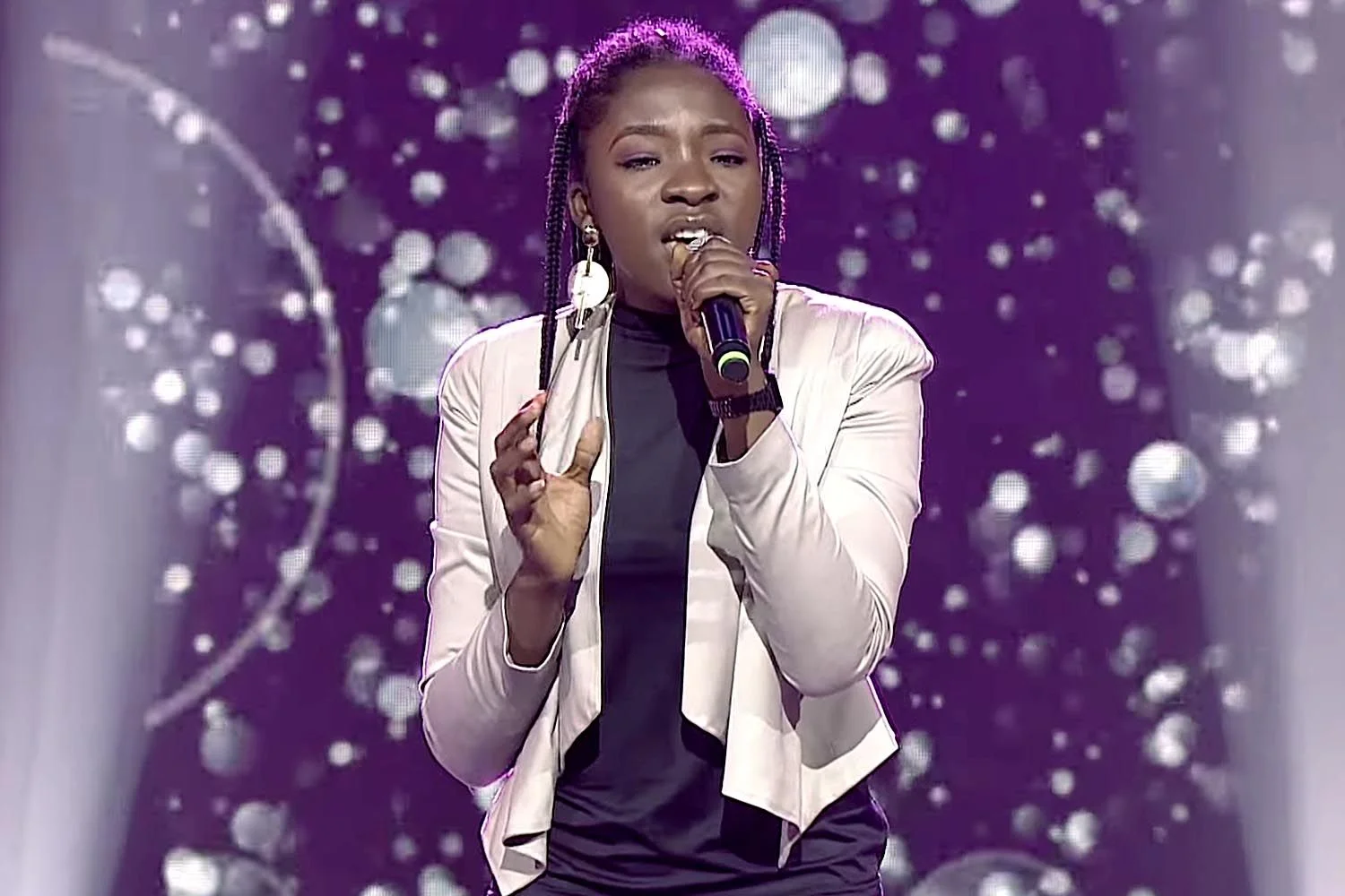 Ifunanya Nwangene performing on stage, singing passionately with microphone in hand, spotlight illuminating her face.