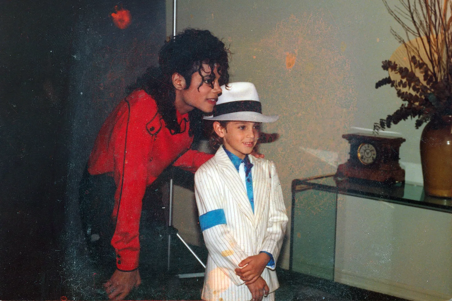 Michael Jackson posing with a young fan dressed in a miniature version of his signature fedora and sunglasses, smiling for a photo.