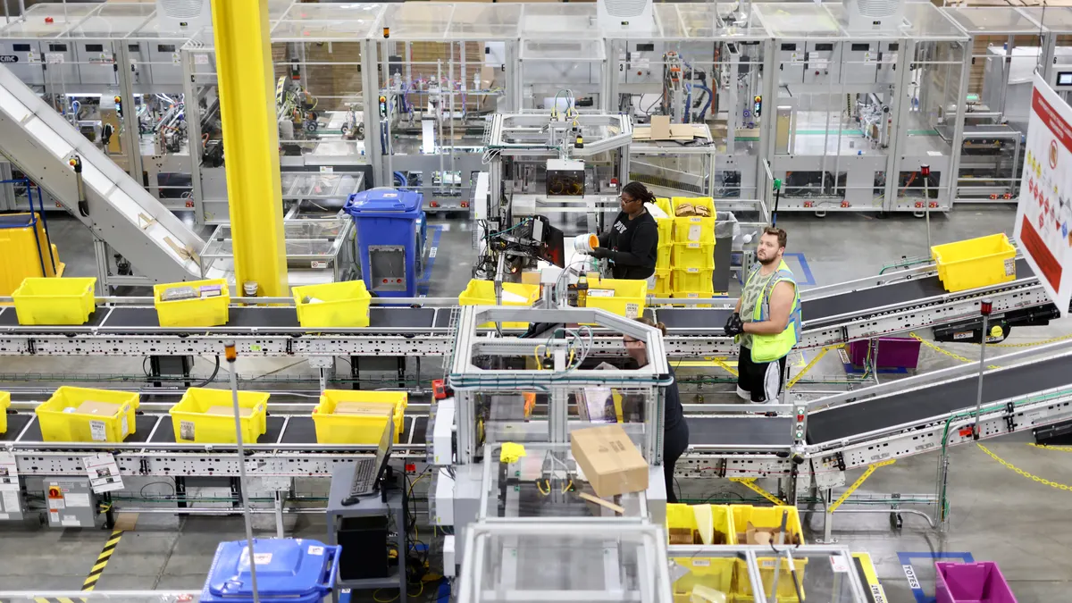 Amazon warehouse worker standing beside an autonomous robot inside a fulfillment center.