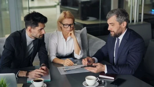 A financial planner seated at a desk reviewing printed documents with two clients