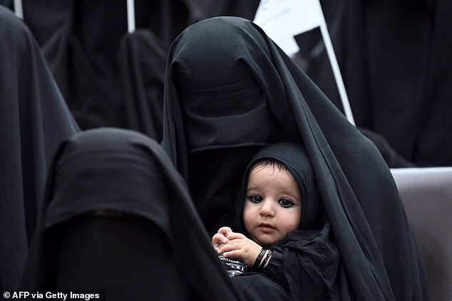 A veiled woman carries her child as they listen a speaker before a pro-Taliban rally at the Shaheed Rabbani Education University in Kabul on September 11, 2021